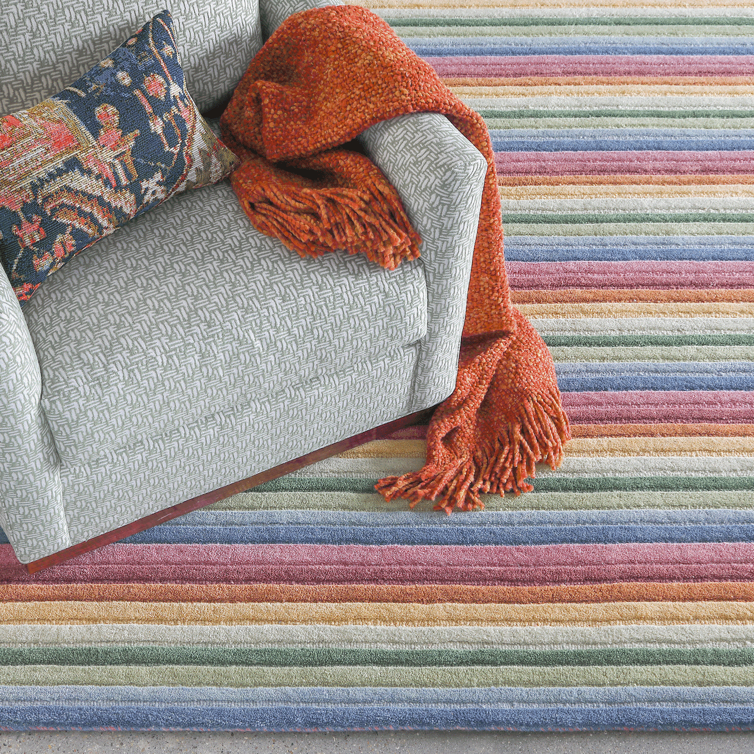 Colorful striped rug with a gray chair and orange throw