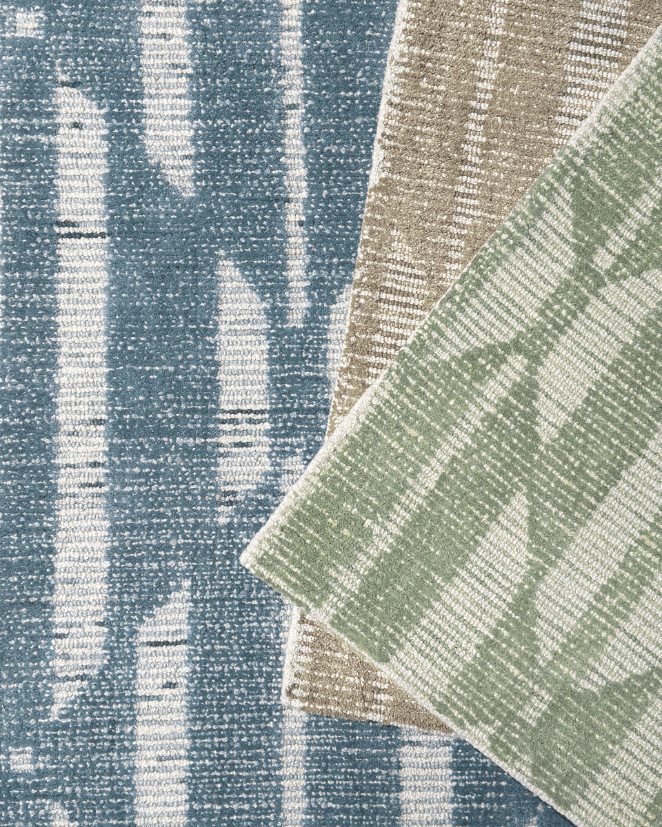 stack of geometric rugs in blue, natural, and sage colors